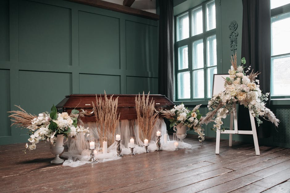 A floral arrangement featuring large white roses, delicate white orchids, and flowing greenery, set in a white vase on the right. The arrangement is complemented by dried pampas grass and accented by